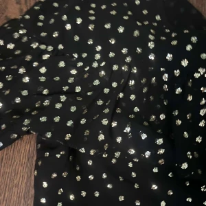 Svart glittrig blus - Supersöt svart blus med glittriga silverprickar. Klänningen har korta puffärmar och rund halsringning. Perfekt för dig som vill sticka ut med lite extra glitter. Lätt och luftig känsla, passar till många tillfällen.