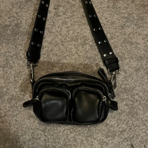 Svart axelväska med nitar och dragkedjor - Väska från Gina tricot, har bara använt 2 gånger💕 ganska liten men ändå rymlig!
