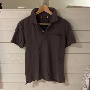 Mörkgrå pikétröja från Morris - Snygg mörkgrå pikétröja från Morris med klassisk krage, knappslå och bröstficka. Perfekt för en clean och stilren look. Tillverkad i mjuk bomull som känns skön mot huden.