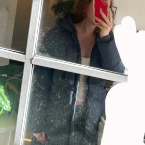 Mörkblå lång pufferjacka - Säljer en mörkblå pufferjacka från Zink med huva och långa ärmar. Jackan har en rak, lite oversized passform, två stora fickor framtill och en bröstficka med dragkedja. Perfekt för kalla dagar och har snygga quiltade detaljer. Väldigt varm!