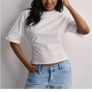 Vit croppad topp med knyt i ryggen - Säljer en stilren vit croppad topp med korta ärmar och hög hals. Toppen har en snygg öppen rygg med breda band som knyts baktill för en cool detalj. Perfekt till jeans eller kjol för en trendig look.