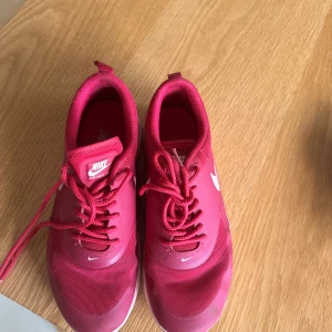 Nike Air Max sneakers i rosa - Snygga Nike Air Max sneakers i en stark rosa färg med vita detaljer och logga. Skorna har snörning, rund tå och en synlig Air Max-sula som ger extra komfort. Ovandelen är i mesh och syntet, vilket gör dem lätta och andningsbara. Perfekta för dig som gillar sportig stil.