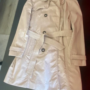 Beige trenchcoat från edc, S - Snygg beige trenchcoat från edc med klassisk krage, knappar och bälte i midjan. Jackan har långa ärmar med knäppning vid ärmslut och ett stilrent, tidlöst snitt. Perfekt för dig som vill ha en clean och chic look.