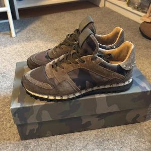 Valentino Rockrunner sneakers camouflage - Snygga Valentino Rockrunner sneakers i camouflage-mönster med bruna och gröna toner. Skorna har detaljer i mocka och skinn, coola nitar runt hälen och sula samt klassisk snörning. Tre nitar saknas vilket inte är någon större märkvärdighet därav priset. Storlek 42 passar även 43. Hör av dig vid frågor