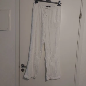 Vita linnebyxor med snörning - Säljer ett par vita linnebyxor med avslappnad passform och resår i midjan samt snörning. Byxorna är raka i modellen och har en luftig känsla, perfekta för varma dagar. Materialet är linne och färgen är helt vit.