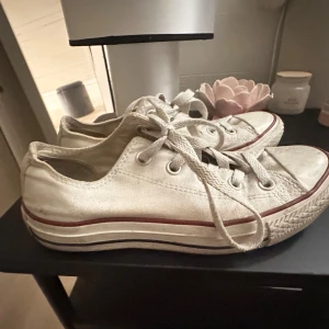 Vita Converse sneakers strl 36.5 - Klassiska vita Converse sneakers i canvas med lågt skaft och snörning. Skorna har rund tå, platt sula och den ikoniska röda randen längs sulan. Perfekta för en avslappnad och cool stil.