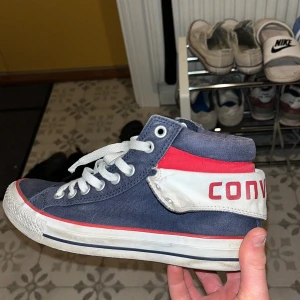 Converse All Star blå och röda sneakers - Säljer ett par Converse All Star sneakers i canvas med högt skaft. Skorna är blå med röda och vita detaljer, vit sula och snörning framtill. Stor logga baktill och klassisk rund tå. Perfekta för dig som gillar streetstyle och vill sticka ut lite extra. Dem är strl 40 men jag själv har 42 och dem passat mig.