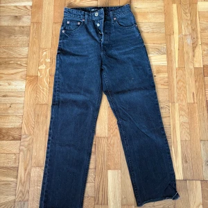 Svarta raka jeans från Zara, strl 34 - Säljer ett par svarta jeans från Zara i storlek 34. Jeansen har raka ben, hög midja och råa kanter nertill för en cool vibe. Klassisk femficksmodell med knappgylf. Perfekta till sneakers eller boots.