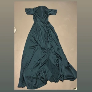 Mörkgrön lång satinklänning från SHEIN - Klänningen har omlott-design med v-ringad hals och korta ärmar. Dragkedja i ryggen. Perfekt för dig som vill sticka ut. Skönt och snyggt material! Slit hela vägen på benen för en elegant look. 