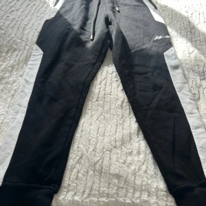 Svarta mjukisbyxor Elly Pistol S - Svarta mjukisbyxor från Elly Pistol i storlek S med vita sidopaneler och snörning i midjan. Byxorna har en sportig look och är tillverkade i mjukt material för maximal komfort. Perfekta för chill eller träning.