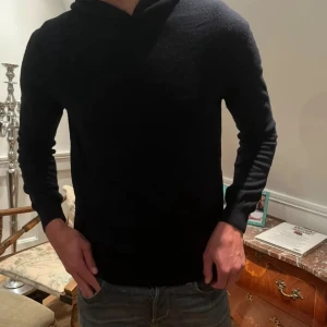 Svart hoodie i kashmir från Oscar Jacobsson - Mjuk och stilren svart hoodie från Oscar Jacobsson nypris 1400kr i lyxig kashmir. Tröjan har lång ärm, klassisk huva och en clean look utan tryck eller detaljer. Perfekt för dig som gillar en enkel men exklusiv stil.