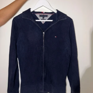 Marinblå kofta från Tommy Hilfiger XS - Snygg marinblå kofta från Tommy Hilfiger i premium bomull. Dragkedja framtill, liten broderad logga på bröstet och ribbade muddar. Perfekt för lager-på-lager och stilren look. 