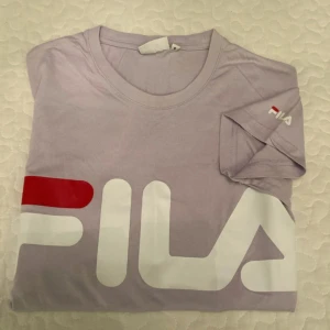 Ljuslila FILA t-shirt med stor logga - Säljer en ljuslila t-shirt från FILA i bomull med stor vit och röd logga framtill. Klassisk rund hals och korta ärmar. Perfekt för dig som gillar sportiga och stilrena plagg med tydlig branding.
