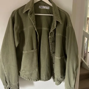 Grön jeansjacka Zara - Säljer en olivgrön jeansjacka från Zara. Jackan har två stora fickor framtill, klassisk krage och knappar längs hela framsidan. Perfekt att slänga på sig över en hoodie eller t-shirt för en chill look.