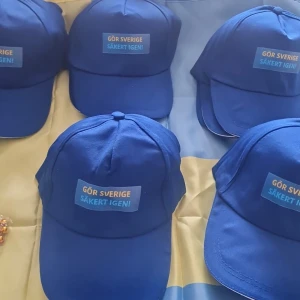 Blå keps med text 'Gör Sverige säkert igen!' - Snygg blå keps med böjd skärm och tryckt text på framsidan: 'Gör Sverige säkert igen!' i gult och blått. Klassisk modell med paneler och knapp på toppen. Perfekt för dig som vill sticka ut och visa budskapet. Justerbar baktill för bästa passform.