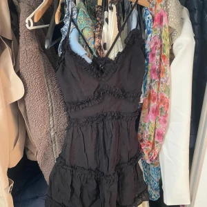 Svart volangklänning med smala axelband - Supersöt svart kortklänning med smala axelband och volangdetaljer. Klänningen har en feminin v-ringning och flera lager volanger som ger en lekfull känsla. Perfekt för dig som gillar en romantisk och trendig stil. De står M som storlek men är mindre enligt mig 