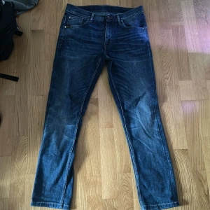 Blå jeans - Snygga blå jeans med klassisk femficksdesign. Jeansen har en mörk tvätt med slitningar och kontrastsömmar. Perfekta för en avslappnad och stilren look.