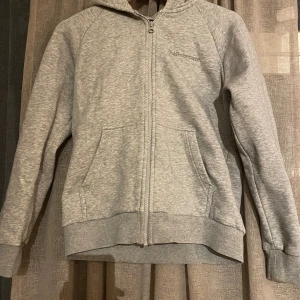 Grå hoodie från Peak Performance XS - Mysig grå hoodie från Peak Performance i storlek XS. Tröjan har dragkedja framtill, två fickor och broderad logga på bröstet. Perfekt för chill dagar eller när du vill vara extra bekväm. Huva och ribbade muddar ger en skön passform. Knappt använd pågrund av att storleken var för liten. Nypris ligger mellan 1200-1400