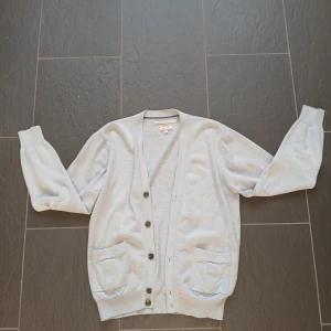 Ljusblå kofta från GANT i kashmirmix - Snygg ljusblå kofta från GANT i mjuk pima bomull och kashmir. Klassisk modell med knappar framtill, två fickor och ribbade muddar. Perfekt för lager-på-lager och chill stil. Storlek m men passar även s. 