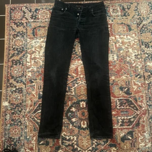Nudie Jeans Grim Tim - Ett år par svarta nudie jeans i modellen grim tim  Mått: midja 39cm, längd 105cm, ben öppning 16cm, innerbenslängd 78-79cm, har ett hål i vänster ficka se sista bilden. Egentligen w32 men sitter som w30