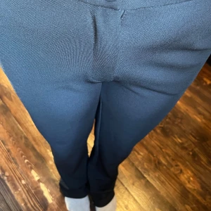 Svarta kostymbyxor med rak passform - Snygga svarta kostymbyxor med klassisk rak passform och mid waist. Byxorna har diskret gylf och är tillverkade i ett slätt tyg som ger en stilren look. Perfekta för dig som gillar en clean och tidlös stil.