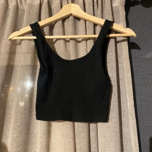 Svart ribbad croppad topp Gina Tricot - Säljer en svart croppad linne-topp från Gina Tricot i storlek XS. Toppen är ribbad och har breda axelband samt rundad halsringning. Perfekt att styla med jeans eller kjol för en enkel och snygg look.