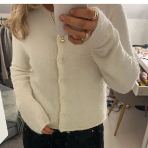 Vit kofta i mjuk ullmix - Supermysig vit kofta med rund hals och knappar framtill. Tröjan är stickad i en fluffig ullmix och har långa ärmar. Perfekt för lager-på-lager och ger en clean look till alla outfits.