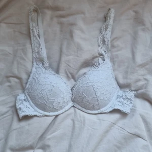 Vit spetsig push-up bh med blommönster - Säljer en vit bh med vacker spets och blommigt mönster. Bh:n har justerbara axelband och hakknäppning bak. Kuporna är vadderade för extra push-up-effekt och spetsdetaljerna ger en romantisk vibe.