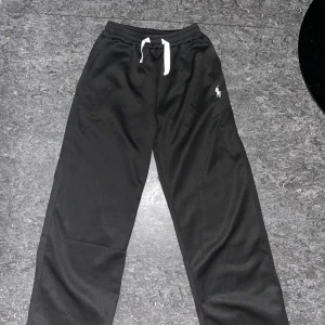 Svarta mjukisbyxor från Polo Ralph Lauren - Oanvända Svarta mjukisbyxor från Polo Ralph Lauren med vit broderad logga på benet och vit snörning i midjan. Byxorna har avslappnad passform och resår i midjan för extra komfort. Perfekta för chill dagar eller när du vill vara bekväm men ändå stilren.