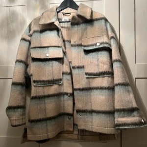 Rutig overshirt från Pimkie i ullmix - Snygg overshirt i beige, blått och grått rutmönster från ASOS. Jackan har stora bröstfickor med knappar, klassisk krage och är tillverkad i en mjuk ullblandning. Perfekt för lager-på-lager och chill stil.