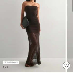 Brun axelbandslös långklänning - Snygg brun axelbandslös långklänning med figurnära passform. Klänningen har en transparent, plisserad nederdel som ger en cool och trendig look. Perfekt för dig som vill sticka ut med en elegant och modern stil.