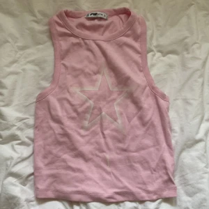 Rosa linnetopp med stjärna från FB Sister - Säljer en ljusrosa ärmlös linnetopp från FB Sister i bomull. Toppen har en vit stjärna tryckt framtill och klassisk rund halsringning. Perfekt för varma dagar och enkel att matcha med jeans eller shorts. Jag säljer den nu för att den inte passar min stil längre. Den har en liten fläck på magen men det går bort enkelt med Vanish🩷✨