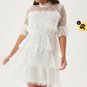 Vit spetsklänning med volanger - Superfin vit studentklänning klänning i spets med volanger och hög hals. Klänningen har halvtransparenta ärmar och överdel, samt flera lager i kjolen som ger en fluffig känsla. Endast använd en gång! 💘