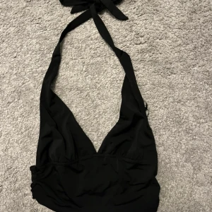 Svart bikiniöverdel med knyt - Snygg svart bikiniöverdel med djup v-ringning och breda band som knyts i nacken. Enkel och stilren design som passar perfekt till stranden eller poolen. Mjuk och bekväm passform.