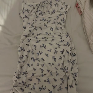 Vit blommig kortklänning från SHEIN - Supersöt vit kortklänning från SHEIN med blått blommönster. Klänningen har en figurnära passform och är perfekt för varma dagar. Materialet är mjukt och stretchigt, vilket gör den bekväm att bära. Perfekt för dig som gillar en romantisk och fräsch stil.