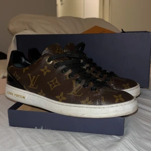 Louis Vuitton monogram sneakers - Snygga Louis Vuitton sneakers i brunt med klassiskt monogrammönster och svarta detaljer. Skorna har svart snörning, vit platt sula och är tillverkade i skinn. Perfekta för dig som vill sticka ut med lyxig streetstyle.