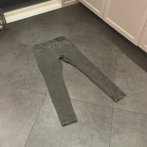 Grå jeans från G-Star RAW, 32/32 - Säljer ett par grå jeans från G-Star RAW i storlek 32/32. Byxorna har en slim passform, klassiska fem fickor och snygga detaljer vid bakfickorna. Tillverkade i bomull med en lätt tvättad look och svarta knappar. Perfekta för dig som gillar stilrena jeans.