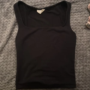 Svart linnetopp från Gina Tricot XS - En svart, stilren linnetopp från Gina Tricot i modellen Basically Basics. Toppen har breda axelband och fyrkantig ringning, perfekt att matcha med jeans eller kjol. Enkel och klassisk design som funkar året runt.