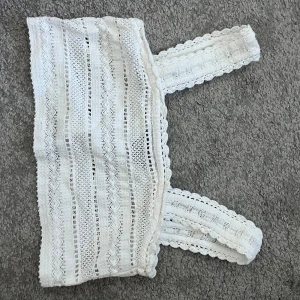 Vit spetsig linnetopp med breda axelband - Superfin vit linnetopp med breda axelband och detaljerad spets. Toppen har virkade ränder och en liten knäppning framtill. Perfekt för varma dagar och ger en romantisk vibe till din outfit.