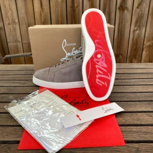 Christian Louboutin grå mocka sneakers - Snygga sneakers  i grå mocka med klassisk röd sula och vita kanter. Skorna har rund tå, snörning och exklusiv känsla. Perfekta för dig som vill sticka ut med lyxiga detaljer och stilren design.