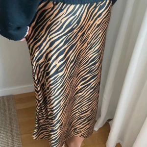 Zebramönstrad långkjol i satinlook - Snygg långkjol med zebramönster i svart och beige. Kjolen har en glansig satinliknande yta och en lätt utsvängd passform. 