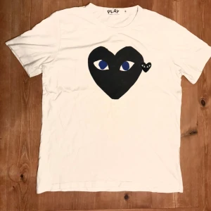 Vit Comme des Garçons Play t-shirt - Vit t-shirt från Comme des Garçons Play med det ikoniska svarta hjärta-trycket med ögon på bröstet. Klassisk passform och rund hals. Perfekt för dig som gillar grisch stilen och vill sticka ut med en cool detalj.