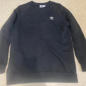 Svart sweatshirt från Adidas, M - En stilren svart sweatshirt från Adidas med klassisk vit logga broderad på bröstet. Tröjan har rund halsringning och långa ärmar. Tillverkad i mjuk bomullsmix. Storlek M men passar även i L.