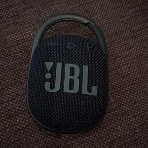 JBL Clip 4 bärbar högtalare blå - Smidig och kompakt JBL Clip 4 högtalare i blå med robust karbinhake. Perfekt för att ta med överallt, med tydliga knappar på ovansidan och slitstarkt tygmaterial. Ger grymt ljud trots sin lilla storlek och är enkel att fästa på väskan.