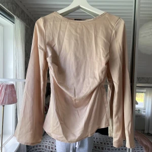Blus i satin - Säljer en beige blus från Boohoo i satinliknande material. Blusen har långa ärmar, rund halsringning och en markerad midja med resår i midjan. 