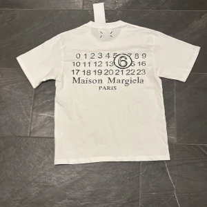 Vit Maison Margiela t-shirt med tryck - Vit t-shirt från Maison Margiela med svart grafiskt tryck och logga på ryggen. 