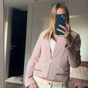 Ljusrosa mockajacka - Ljusrosa mockajacka med silverfärgade dragkedjor framtill och på fickorna, samt dragkedjor vid ärmsluten. Modellen har en clean look och är lätt att styla.