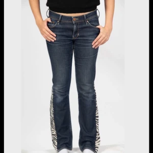 Bootcut jeans med zebradetaljer - Mörkblå bootcut jeans med coola zebramönstrade paneler längs bensluten. Klassisk femficksmodell med normal passform och snygga kontrastsömmar. Perfekta för dig som vill sticka ut med en unik twist på dina jeans. För referens är modellen av byxorna 166 cm.