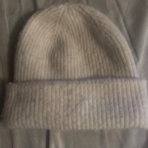 Mössa - Mysig vit mössa med bred uppvikt kant och ribbat mönster. Perfekt för kalla dagar och enkel att matcha med olika outfits. Tillverkad i stickat material som håller dig varm och bekväm.