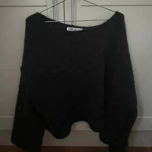 Grå off shoulder stickad tröja Zara - Mysig svart stickad tröja från Zara med croppad passform och bred halsringning. Tröjan har långa ärmar och en fluffig känsla, perfekt för kyliga dagar. Enkel att styla med både jeans och kjol.
